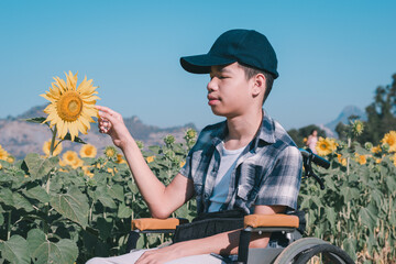 Fototapeta premium Asian Special need child on wheelchair smiling with admire outdoors nature and blue sky in the sunflowers field,Lifestyle in education age of disabled kids,Happy disability kid travel concept.