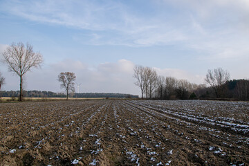 A freshly plowed field prepared for sowing, covered with fresh snow in the Polish countryside in...