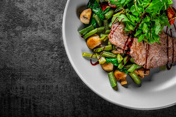 Roastbeef salad with green beans and mushroom in a bowl on Dark grey black slate background