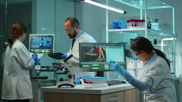 Scientist team checking virus development using high tech writing analysis results on computer in modern equipped lab at night. Doctors examining vaccine evolution with special tools for research.