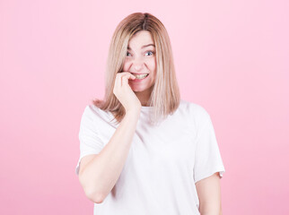 Close up portrait of a worried teenage girl in white t-shirt biting her nails isolated over pink background