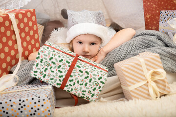 Portrait of a cute little girl child wearing a silver color Christmas hat laying between gift boxes in a decorated house.Merry Christmas and Happy Holidays!