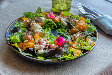 A colorful salad of peppers, fruits, cream, herbs lie on a blue plate. Close-up view