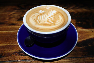 Frothy cappuccino in navy cup and saucer on wooden table