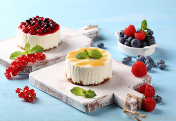 Desserts. Berry and classic cheesecake. Curd dessert with vanilla sponge cake and berry topping. Fresh berry and mint. Raspberries, blueberries on white wooden boards on a blue background. Horizontal