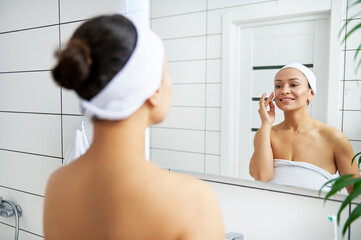 Reflection in the Mirror of a Smiling Woman removing makeup and cleaning her face with micellar water