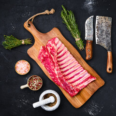 Raw rack of lamb on wooden cutting board with herbs and seasoning