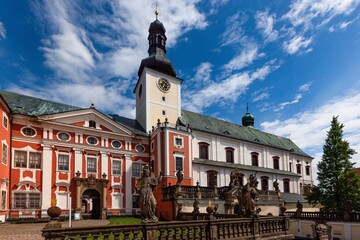 Obraz premium Broumov, Czech Republic - June 17 2020: The Benedictine monastery with red and white facade and the church of St Adalbert from 14th century. Sunny summer day with blue sky and white clouds.