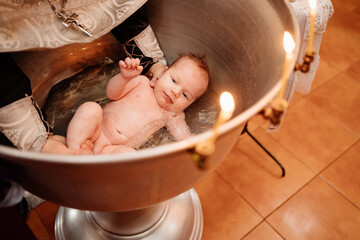 a child is lowered into the water in a font at a Christian baptism in the church