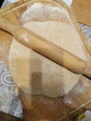 raw dough rolled out with a wooden rolling pin on a light table