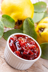Homemade quince jam in a glass jar on an old wooden background. Fresh quince fruits and leaves and quince jam.
