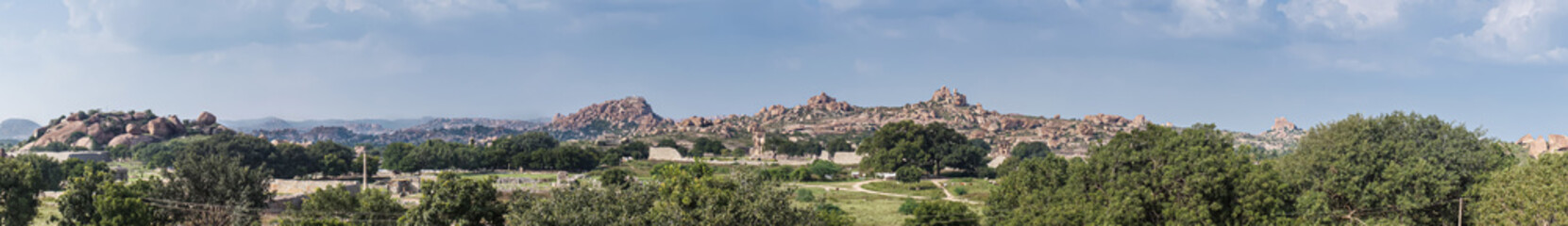Fototapeta na wymiar Hampi, Karnataka, India - November 4, 2013: Royal Enclosure. Panorama shot of the scenery around and above with the Mohammadan Watch Tower about in center. Rocky hills under blue sky. Green vegetation