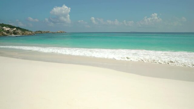 Exotic beach by the ocean with rolling waves on the sandy shore and blue sky. 
