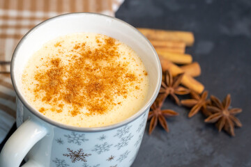 Close up white cup of salep milky hot drink of Turkey with cinnamon powder healthy spice on black wooden background (Sahlep - salep)