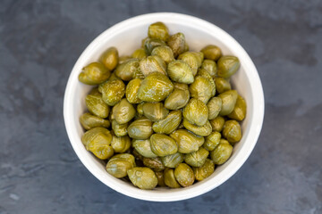 Pickled capers in a glass bowl on a dark background, top view close up (Turkish name; kapari)