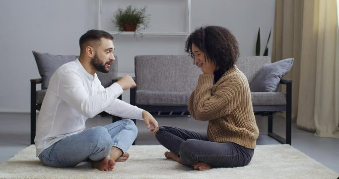 Multiethnic young couple sitting on floor near couch sofa curly woman wife and caucasian husband man quarreling shouting outraged together sort out relationship, separation divorce problem concept