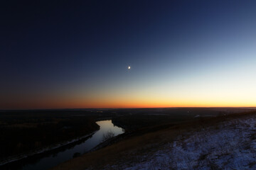 Young moon over the river at dusk. Bright evening sky after sunset.