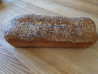 Homemade, molded, browned, crunchy bread sprinkled with poppy seeds and white sesame seeds. A natural, fresh, delicious loaf. Tasty, freshly baked batch on a brown, wooden, rustic table. Close-up view