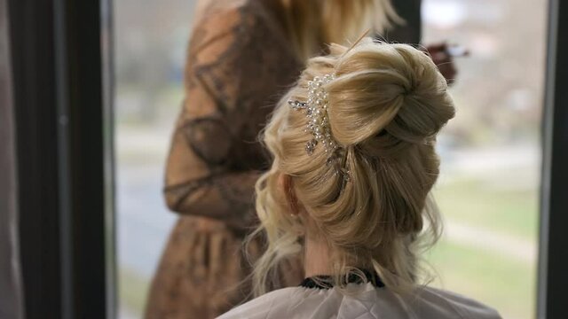 Young bride with beautiful hairdo getting ready with help of visagist