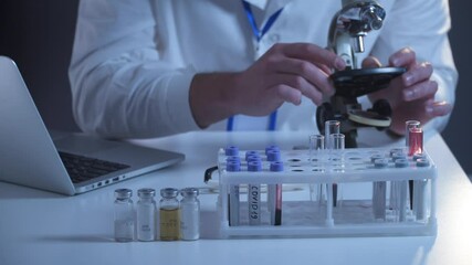 Scientist in lab coat and eyeglasses working at workplace with laptop in laboratory. Male doctor researcher are doing investigations with microscope and laptop. Microbiologists in laboratory - Powered by Adobe