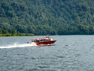 Fototapeta premium a red pleasure boat sails on the lake next to the mountain