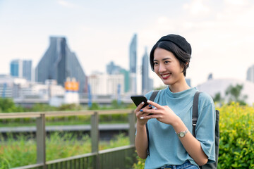 5G smart communication technology makes people comfortable. Cheerful girl using a cellular mobile phone on a sidewalk. Woman having fun with smartphones in garden park. Living in the capital city

