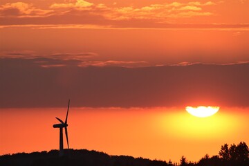 Fototapeta na wymiar Silhouette of a wind turbine at sunset with red sky, environmentally friendly energy production from regenerative sources.