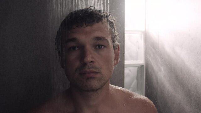 Slow motion close-up shot of a man looking to the camera while taking a morning shower.
