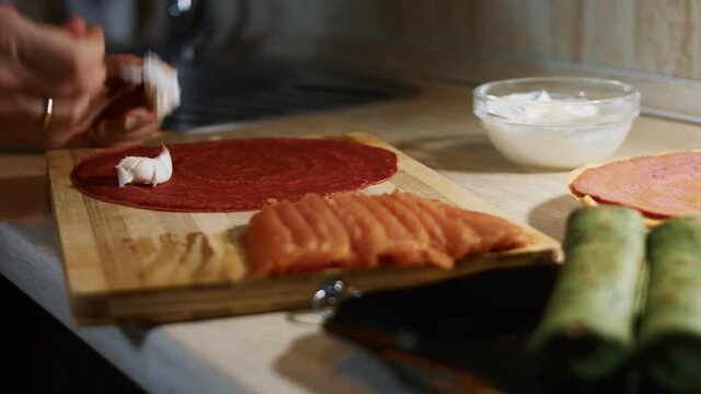 Thin tasty colorful pancakes. Close-up of woman's hand spreading Philadelphia cream cheese as filling on red pancake on a wooden board. 4K video.