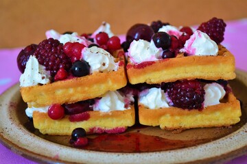 Close-up of a waffle filled with cream, cherries and berries on a pink cloth with white dots