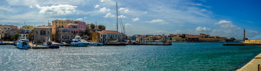 Obraz premium A panorama view from the inner harbour of Chania, Crete looking out to the harbour entrance on a bright sunny day