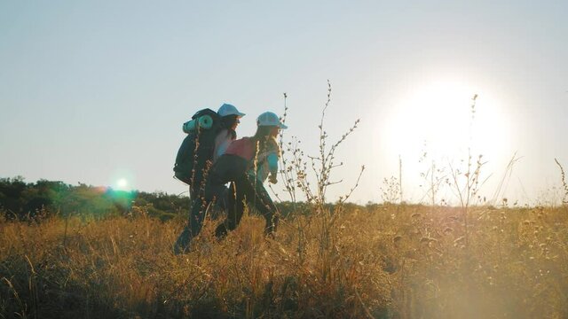 Mother and daughter with backpacks running through the meadow at sunset. Family tourism concept.