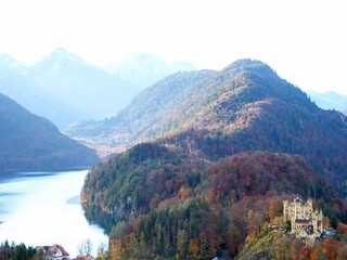 Panoramablick über das Gebiet von Schwangau mit Schloss Hohenschwangau umgeben von bunten Herbstwäldern und vor der Kulisse der bayerischen Alpen.