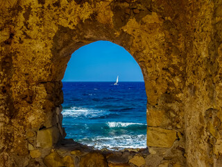 A glimpse of the Mediterranean framed by an opening in the sea wall of Chania harbour, Crete on a bright sunny day