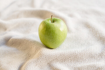 Close-up of single green juicy apple on the table with white tablecloth. Food photography using natural window light. Eating green apples helps increasing the body's metabolism.