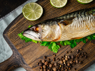 Appetizing cold smoked mackerel with ingredients on a cutting board. On dark wooden background