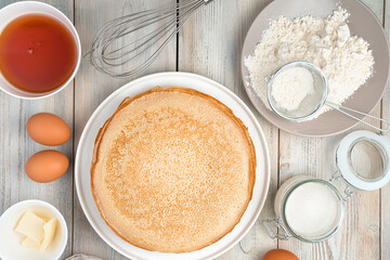 Pancakes on a flat white plate, egg, sugar and napkin on a light background. Top view, horizontal orientation.