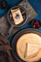 Pancakes with frozen berries on wooden boards on a blue background. Side view, vertical orientation. Concept of culinary backgrounds, Maslenitsa.