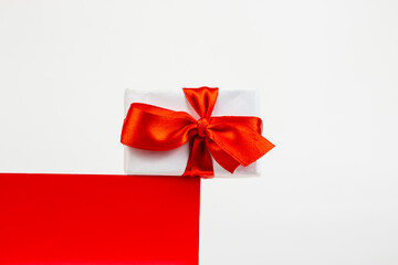 Gift box with a red bow on red cube shape podium. Minimal Christmas holiday composition on white background with copy space
