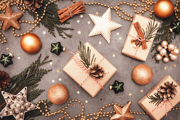 Fototapeta na wymiar Christmas and New Year holiday decorations in green and golden colors on gray concrete backdrop. Craft handmade gift boxes, golden balls, stars and cones. Flat lay style.