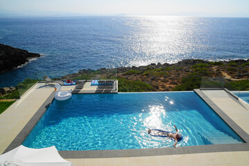 Fototapeta na wymiar Man floating in an infinity pool in front of Aegean sea