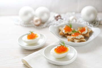 Red caviar on halved eggs and star shaped canapes, white table with light Christmas decoration for a festive holiday buffet, copy space, selected focus