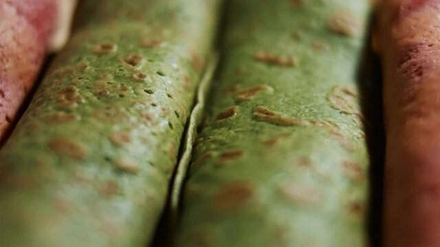 Thin tasty colorful pancakes. Macro view of red and green rolled pancakes with cream cheese and salmon filling on a dish. 4K video.