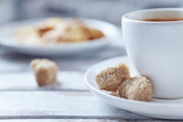 Cup of coffee and brown sugar cubes ( focus on sugar) on bright wooden background. Close up.	
