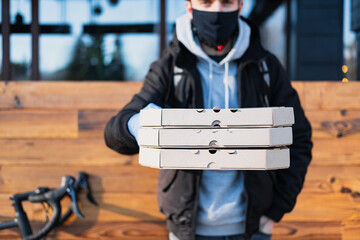 Delivery person holds pizza boxes in a stretched out hand. Food delivery, bicycle courier at work, takeaway catering concept