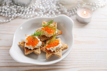Red caviar canapes on toasted bread in star shape with cream and dill garnish on a white plate,...