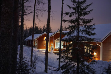 Illuminated cabins at night, viewed through a Scandinavian Forest