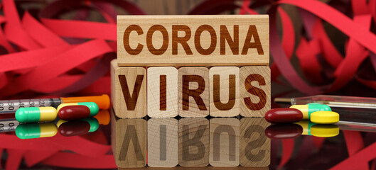On the surface are visible tablets, a syringe, wooden dies and their reflections on which it is written - CORONA VIRUS