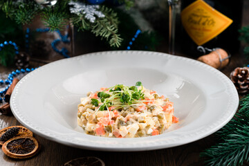 Christmas and New year Olivier salad, traditional Russian food, green tree branch on wooden rustic table, salad Olivier with vegetables and meat. Winter Christmas salad