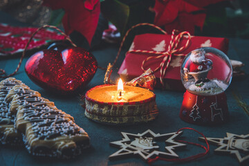 Christmas candle with gingerbread cookies, decorations and poinsettia plant on a dark green background